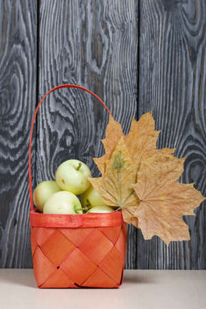 Apples in a red wicker basket. Nearby are dried maple leaves. Fruit harvest.の写真素材