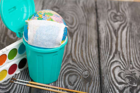 Globe with medical mask. Lies in a trash can. Nearby watercolors and brushes. Academic year during...