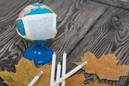 Globe with medical mask. Nearby are pencils and dried maple leaves. Academic year during the...