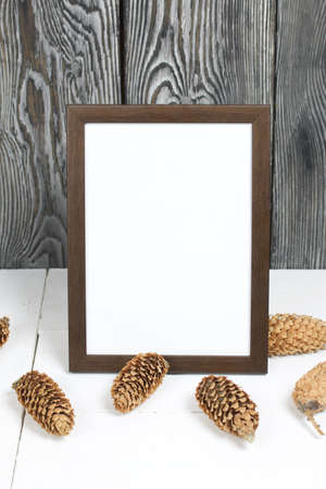 Wooden photo frame with a white field for an inscription or a picture. Nearby are fir cones.