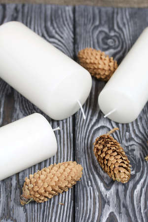 Three white candles lie on painted pine boards. Spruce cones are spread out nearby.の写真素材