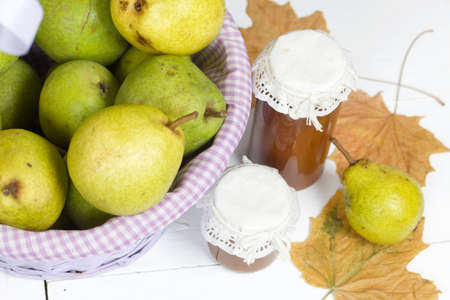 Ripe pears of the new harvest in a wicker basket. On boards painted white. Jam in jars, dried maple leaves.の写真素材