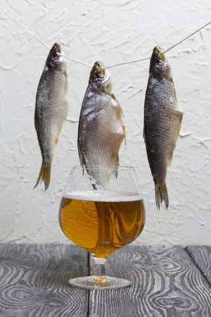 Dried river fish hangs on a rope. There is a glass of beer nearby.