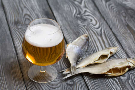 A glass of beer. Dried river fish lies nearby.