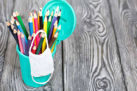 Colored pencils in a pencil holder. They are wearing a medical mask. A pencil case in the form of a trash can. On brushed pine boards painted black and white.の写真素材
