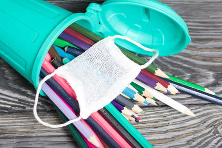 Colored pencils in a pencil holder. They are wearing a medical mask. A pencil case in the form of a trash can. On brushed pine boards painted black and white.の写真素材