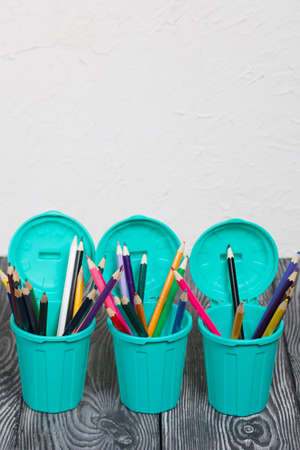 Colored pencils in pencil holders. A pencil case in the form of a trash can. On brushed pine boards painted black and white.の写真素材