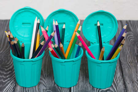 Colored pencils in pencil holders. A pencil case in the form of a trash can. On brushed pine boards painted black and white.の写真素材