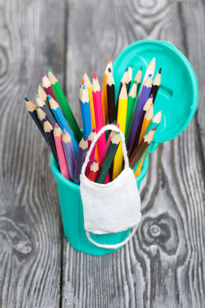 Colored pencils in a pencil holder. They are wearing a medical mask. A pencil case in the form of a trash can. On brushed pine boards painted black and white.の写真素材