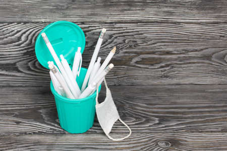 Pencils and ballpoint pens in pencil case. They are wearing a medical mask. A pencil case in the form of a trash can. On brushed pine boards painted black and white.の写真素材