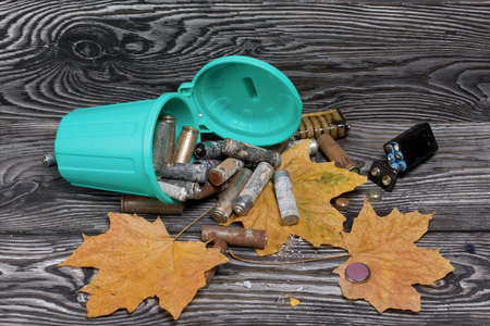 Corroded used batteries. They lie in and around an overturned trash can. Dried maple leaves lie nearby. Disposal of hazardous waste.の写真素材