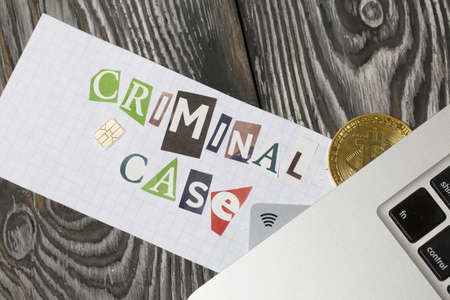 The phrase Criminal case made of letters cut from a magazine and pasted on a sheet of paper. Bitcoin and bank cards are sticking out of the laptop. On brushed pine boards painted black and white.の写真素材