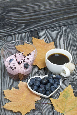 Zephyr in a glass. With biscuit and blueberries. Next to it is a cup of coffee and a saucer of blueberries. Among the maple leaves. On pine boards painted black and white.の写真素材