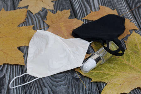 Medical masks in white and black, antiseptic and dried maple leaves. On pine planks painted black and white.の写真素材
