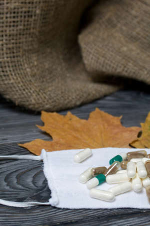 A handful of pills of different colors on a wooden one. On a medical mask. Among the dried up maple leaves. On a pine board surface.の写真素材