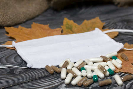 A handful of pills of different colors on a wooden one. Nearby is a medical mask. Among the dried up...