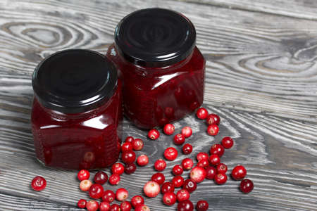 Cranberry jam in glass jars. Cranberries are scattered nearby. On wooden boards with a beautiful texture.の写真素材