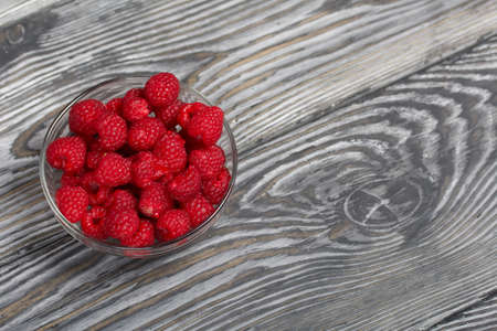 Raspberries in a glass container. On wooden boards with a beautiful texture.の写真素材