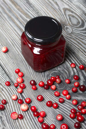 Cranberry jam in glass jars. Cranberries are scattered nearby. On wooden boards with a beautiful texture.の写真素材
