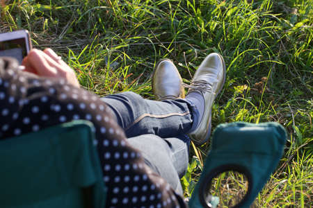The girl is resting in the park. Sits in a camping chair. He is holding a phone in his hands.