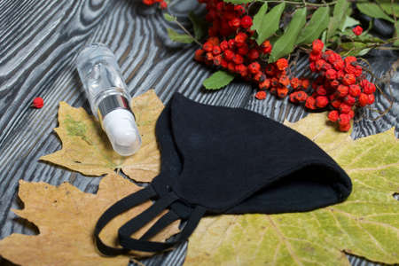 Medical mask and antiseptic. Nearby is a rowan branch and maple leaves. On black pine boards.