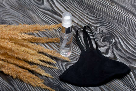 Medical mask and antiseptic. Nearby is a bouquet of dried grass. On black pine boards.の写真素材