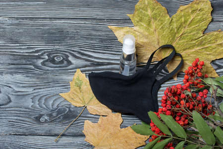 Medical mask and antiseptic. Nearby is a rowan branch and maple leaves. On black pine boards.