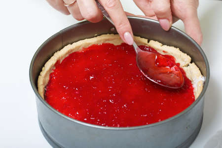 A woman covers coconut flakes in a sponge cake with chocolate ganache with raspberry jelly....