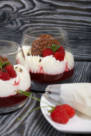 Dessert made from cream cheese with raspberry jelly. Decorated with cookies, raspberries and mint. On pine planks in black.の写真素材