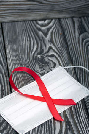 Red Ribbon Symbol for World AIDS Day. Lies on a medical mask. On black pine boards.