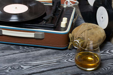 Old turntable. Nearby is a flask and a glass of strong alcohol. Retro party equipment.