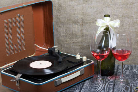 Old turntable nearby two glasses and a bottle of alcohol. Retro party equipment.の写真素材