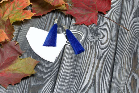Blue tassel earrings. Lie on a medical mask. Around the autumn maple leaves. On pine planks in...