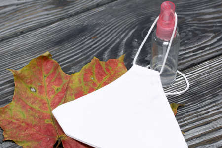 Medical mask and antiseptic. Nearby is a dried autumn maple leaf. On pine planks in black.の写真素材
