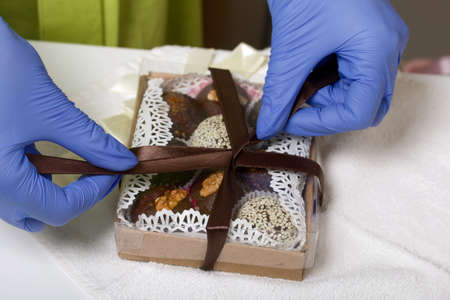 A woman in rubber gloves ties up a cardboard box with dried fruit and nut sweets with tape. Made at home in self-isolation during the epidemic.の写真素材