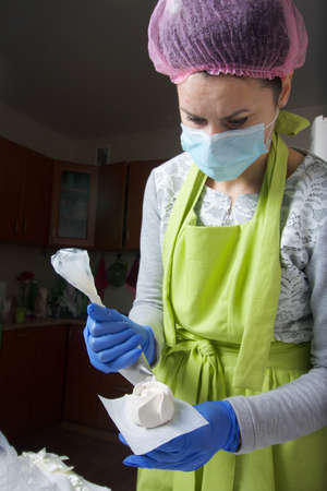 A woman in a medical mask and rubber gloves makes a marshmallow rose at home. Cooking sweets during...