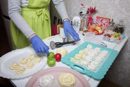 A woman in rubber gloves and a medical mask makes homemade marshmallows. Fresh marshmallows are...