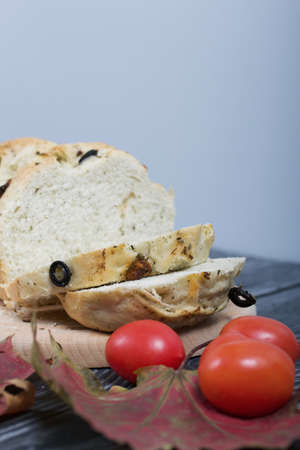 Focaccia bread with olives and sun-dried tomatoes. Several red tomatoes and dried autumn leaves are...