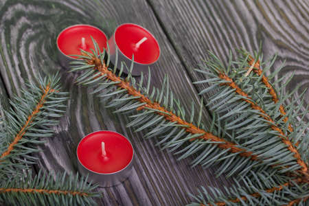 Branches of blue spruce on brushed pine boards. Nearby there are red candles.