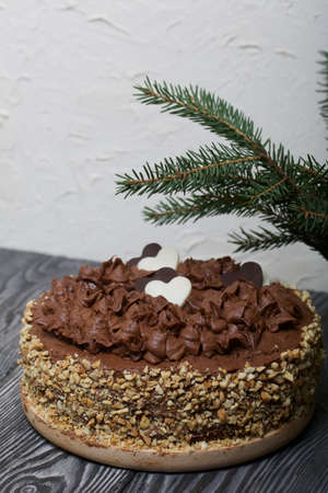 Chocolate cake with cream and peanuts. Decorated with chocolate hearts. Nearby is a spruce branch....