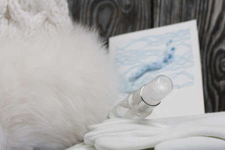 Winter knitted hat with fur and gloves. White. Nearby is a greeting card, a medical mask and an...