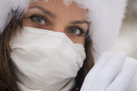 A girl in a medical mask and winter clothes on a walk in the park. Holds a ball of snow in his hand. The ground is covered with the first snowの写真素材