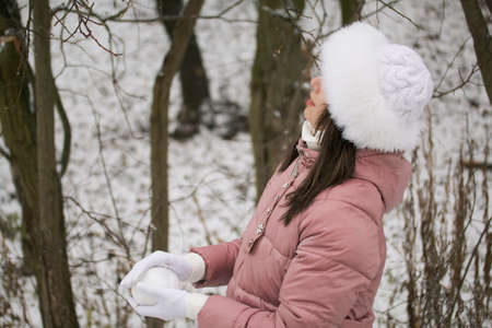 A girl in winter clothes on a walk in the park. He holds a snowball in his hands. The first snow on earth.の写真素材