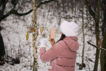 Portrait of a girl in winter clothes. In the foreground are dried leaves on a tree. Close-up shot.の写真素材