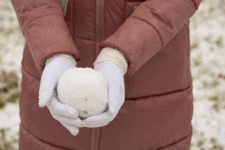 Portrait of a girl in winter clothes on a walk in the park. Snowball in hand. Close-up shot.