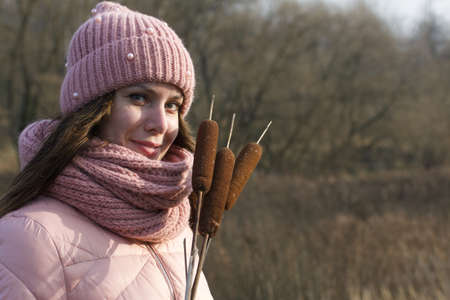 A girl in autumn clothes with a bouquet of reeds in her hands. Walking in nature in the park. Close-up shot.の写真素材