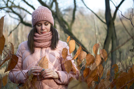 Girl in autumn clothes. Walking in nature in the park. Holds a yellow leaf.の写真素材