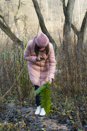 Girl in autumn clothes. Walking in nature in the park. Photographs green branches of a fern.の写真素材