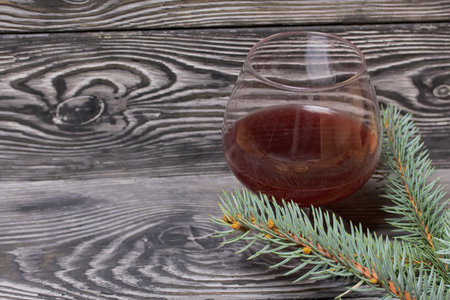 A glass of red wine. Nearby is a spruce branch. On pine boards.の写真素材