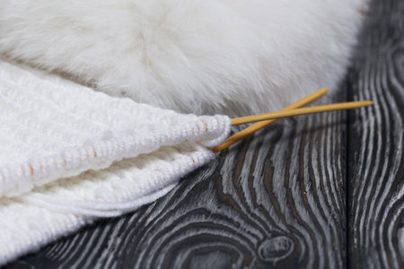Knitting with needles. Wooden knitting needles and white threads. On black pine boards.